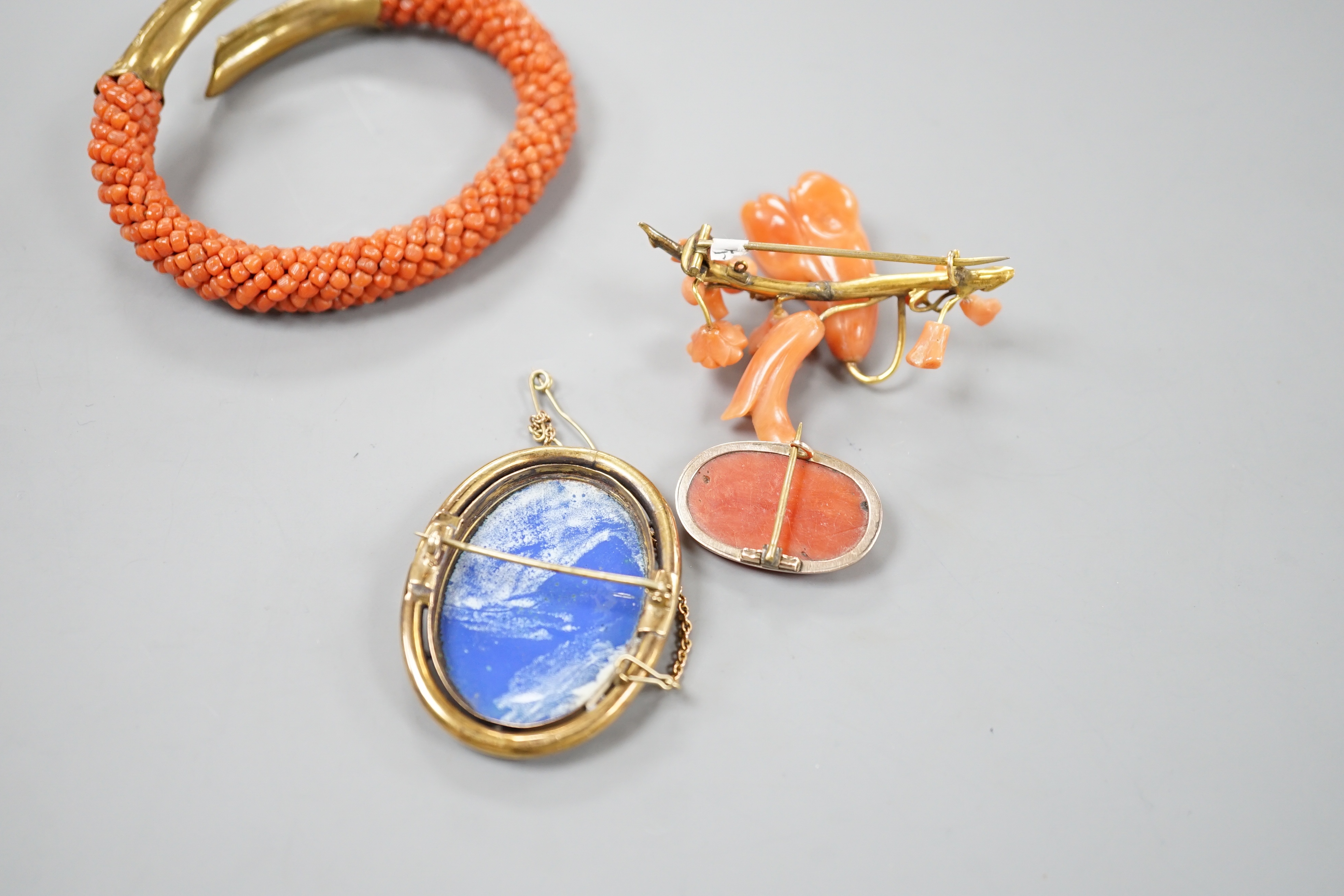 A yellow metal mounted carved coral oval brooch, 30mm, a mounted coral open bangle, a coral brooch and a gilt metal and enamelled brooch.